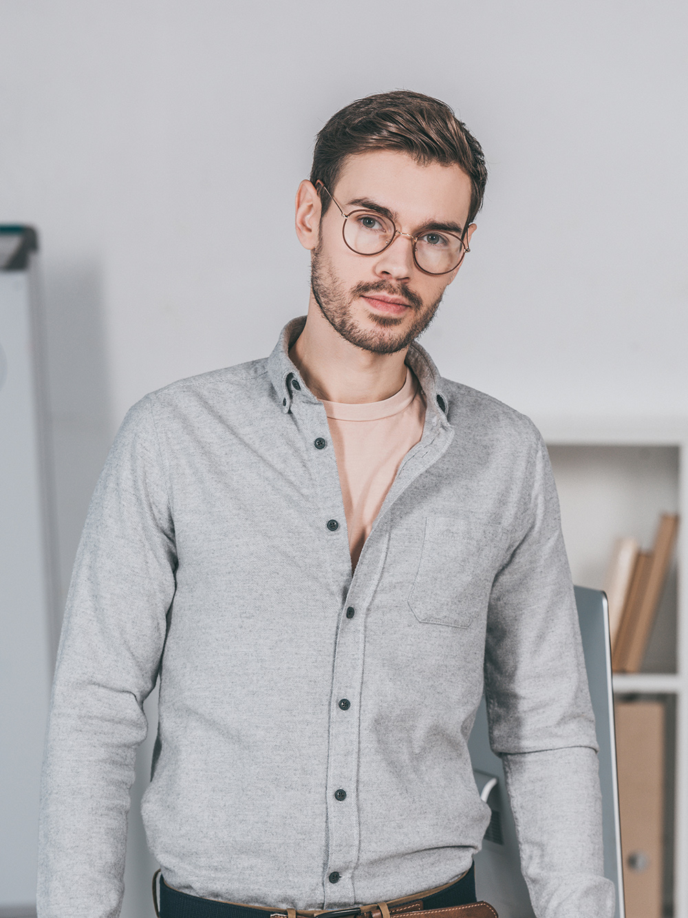 handsome professional young businessman in eyeglasses standing and looking at camera in office